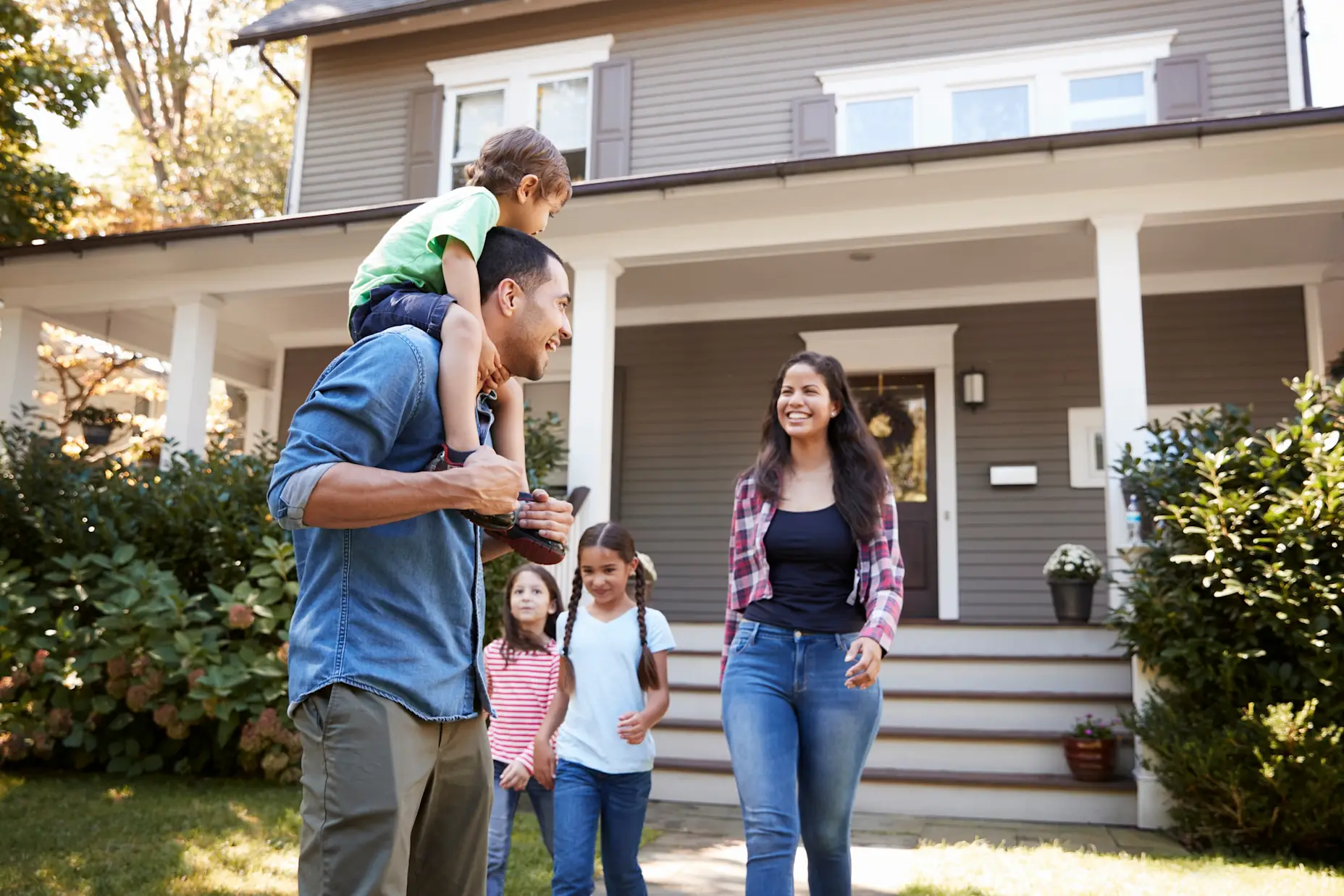 A family outside of their home walking down the sidewalk laughing and smiling.