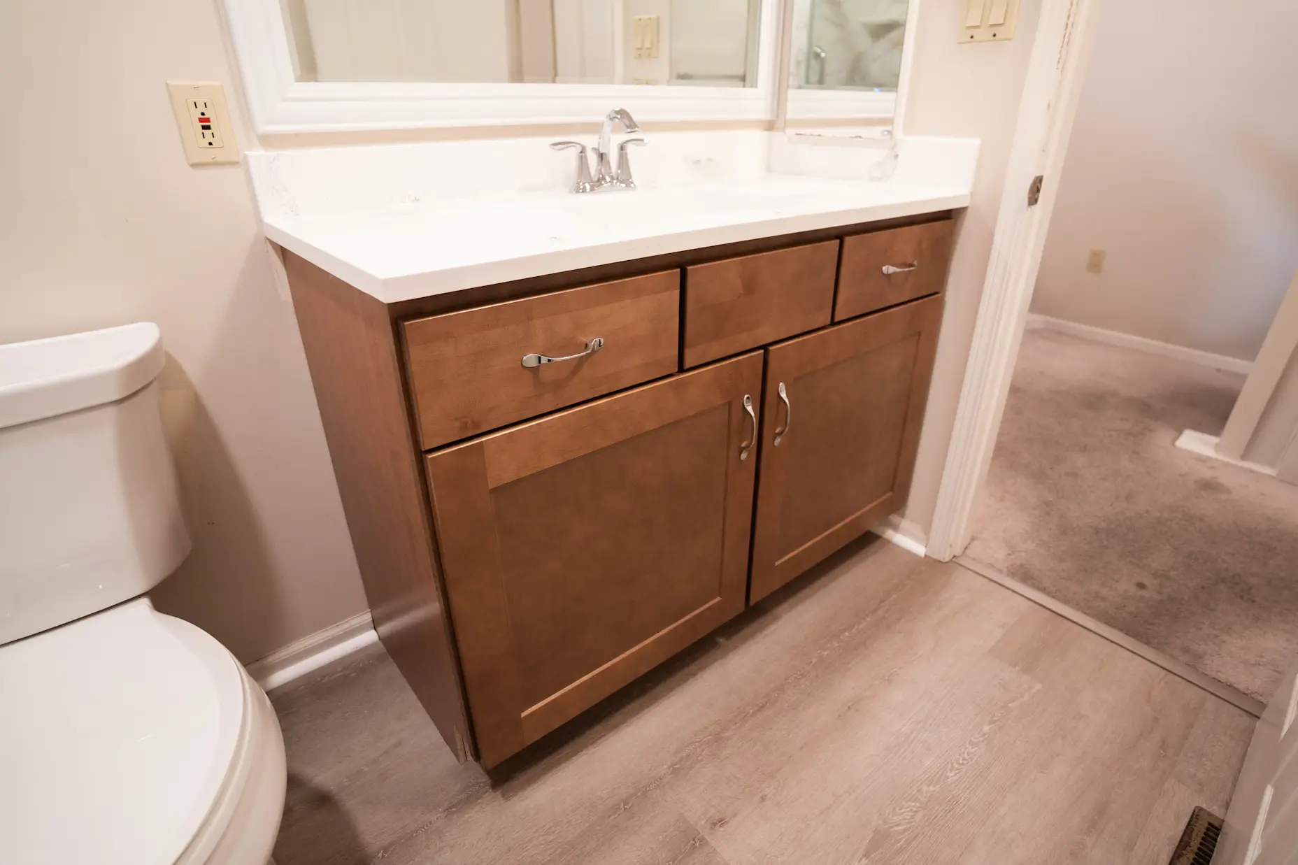 A wooden vanity with chrome hardware and a white countertop.