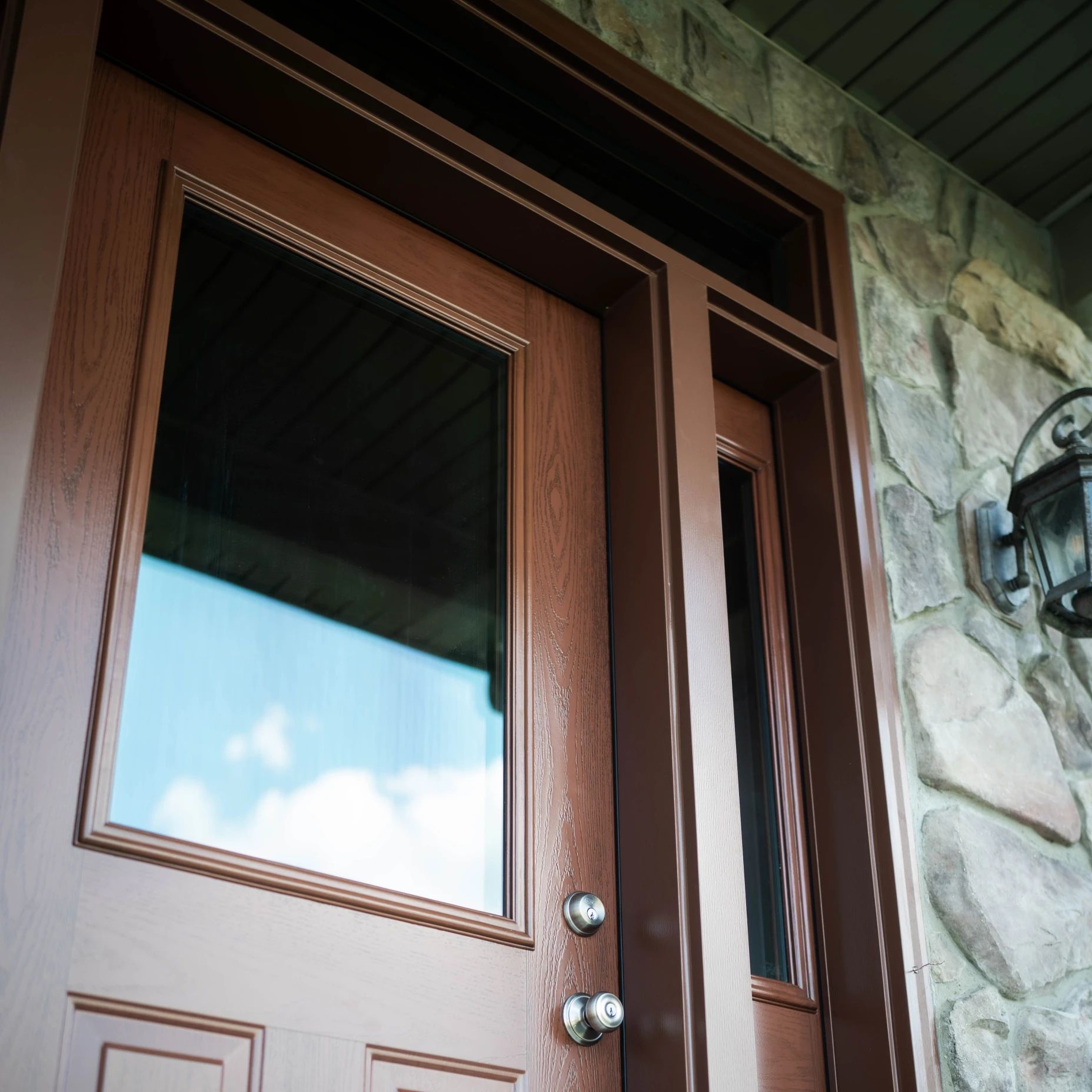 A close up image of a brown woodgrain door with transom and sidelite.