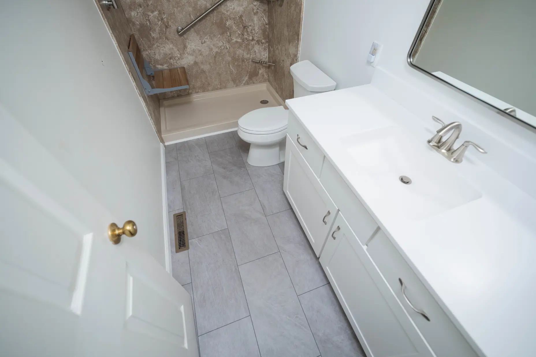 A full bathroom remodel performed by West Shore Home with a new shower unit, toilet unit, vanity, and flooring.