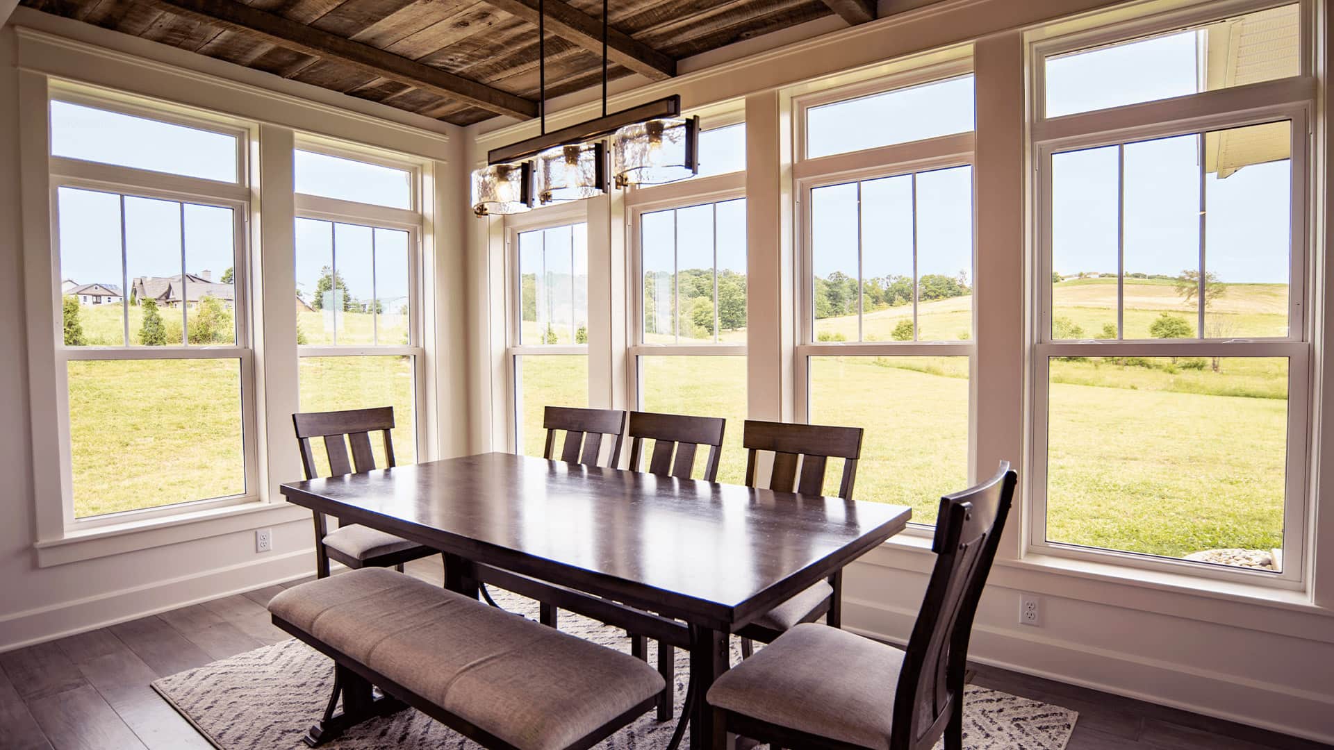 A rustic contemporary dining room with a row of large double-hung windows looking out onto a large field.