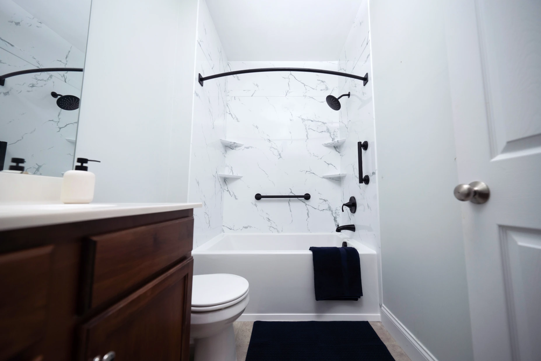 A black and white tub and shower combo with marble design shower walls and black matte grab bars.