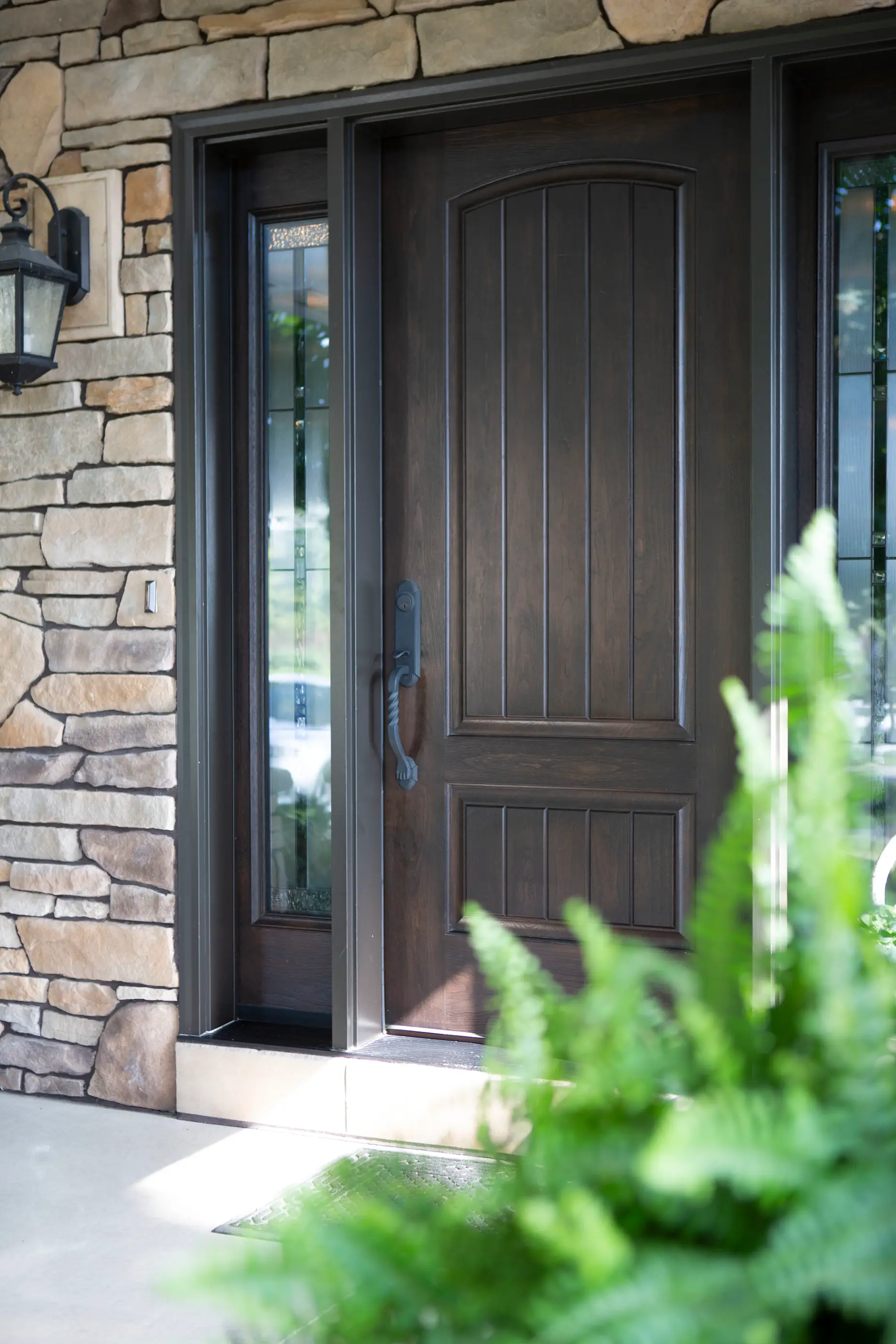 Brown entry door with two sidelights against stone siding.