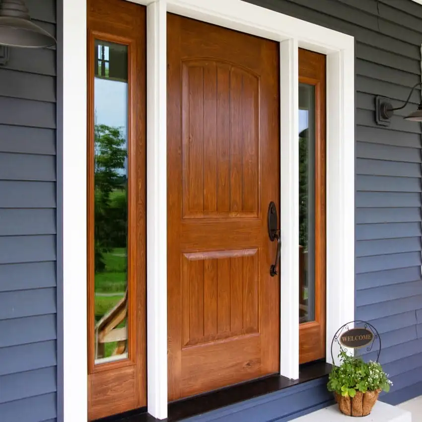 A large wooden entry door on a home with grey siding and a large porch.