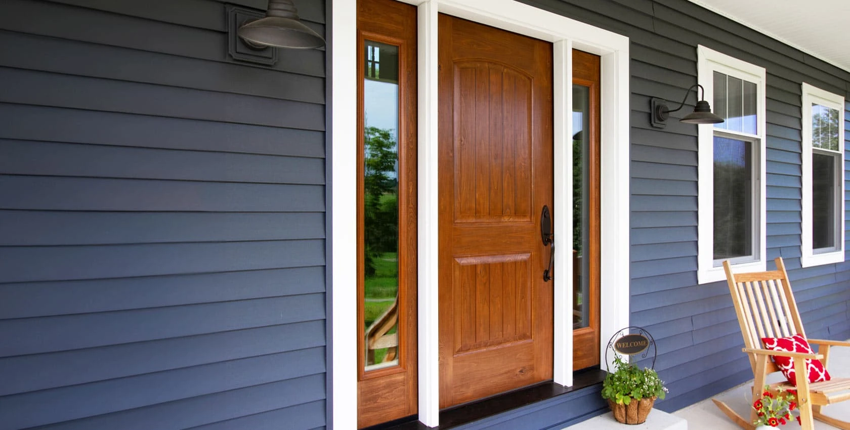 A large wooden entry door on a home with grey siding and a large porch.