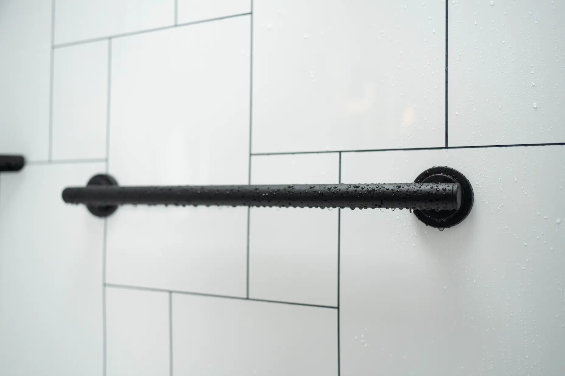 A black matte grab bar on a black and white tile shower wall.