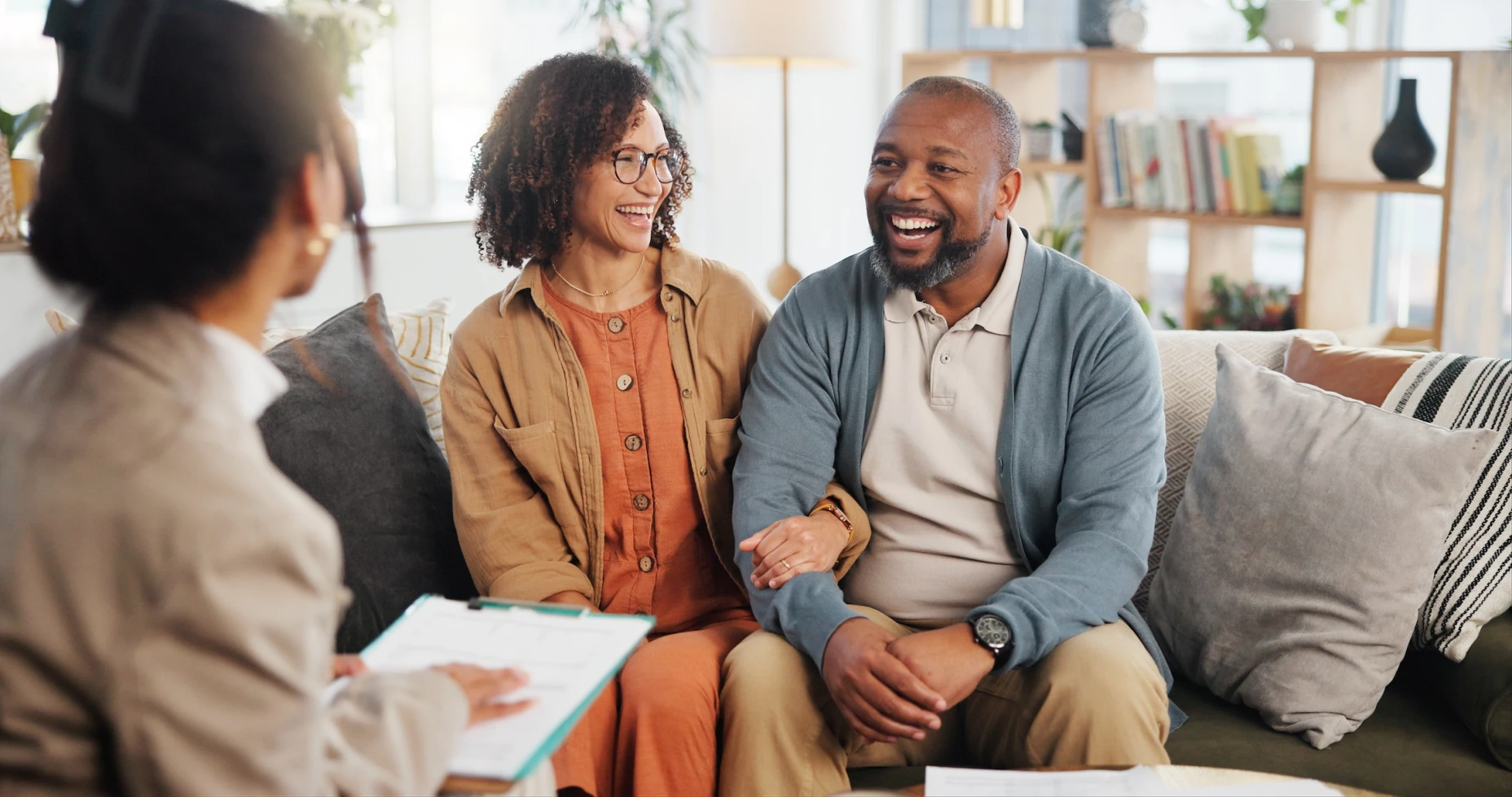 A woman and a man laughing and smiling speaking to a woman holding a clipboard.