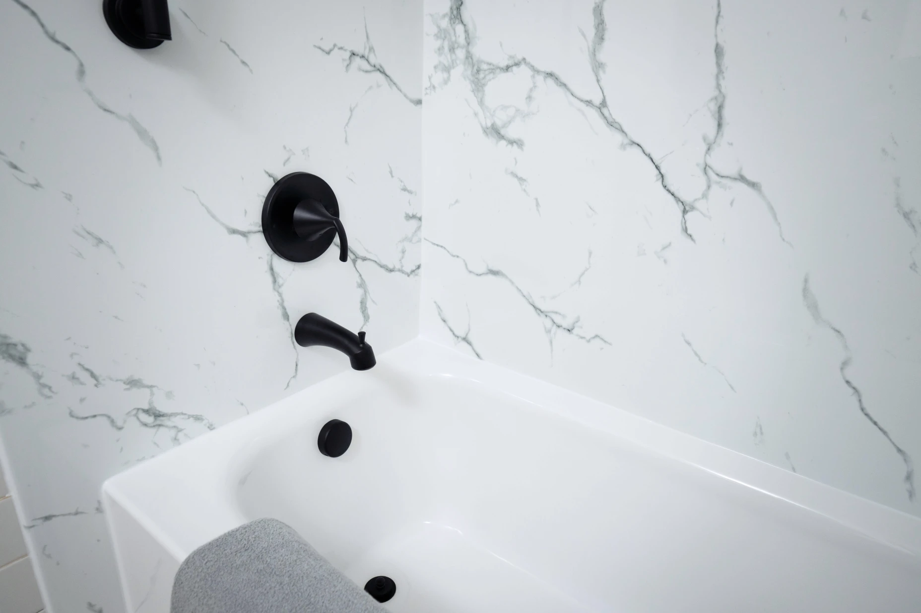 A black and white marble acrylic bathtub with black matte fixtures.