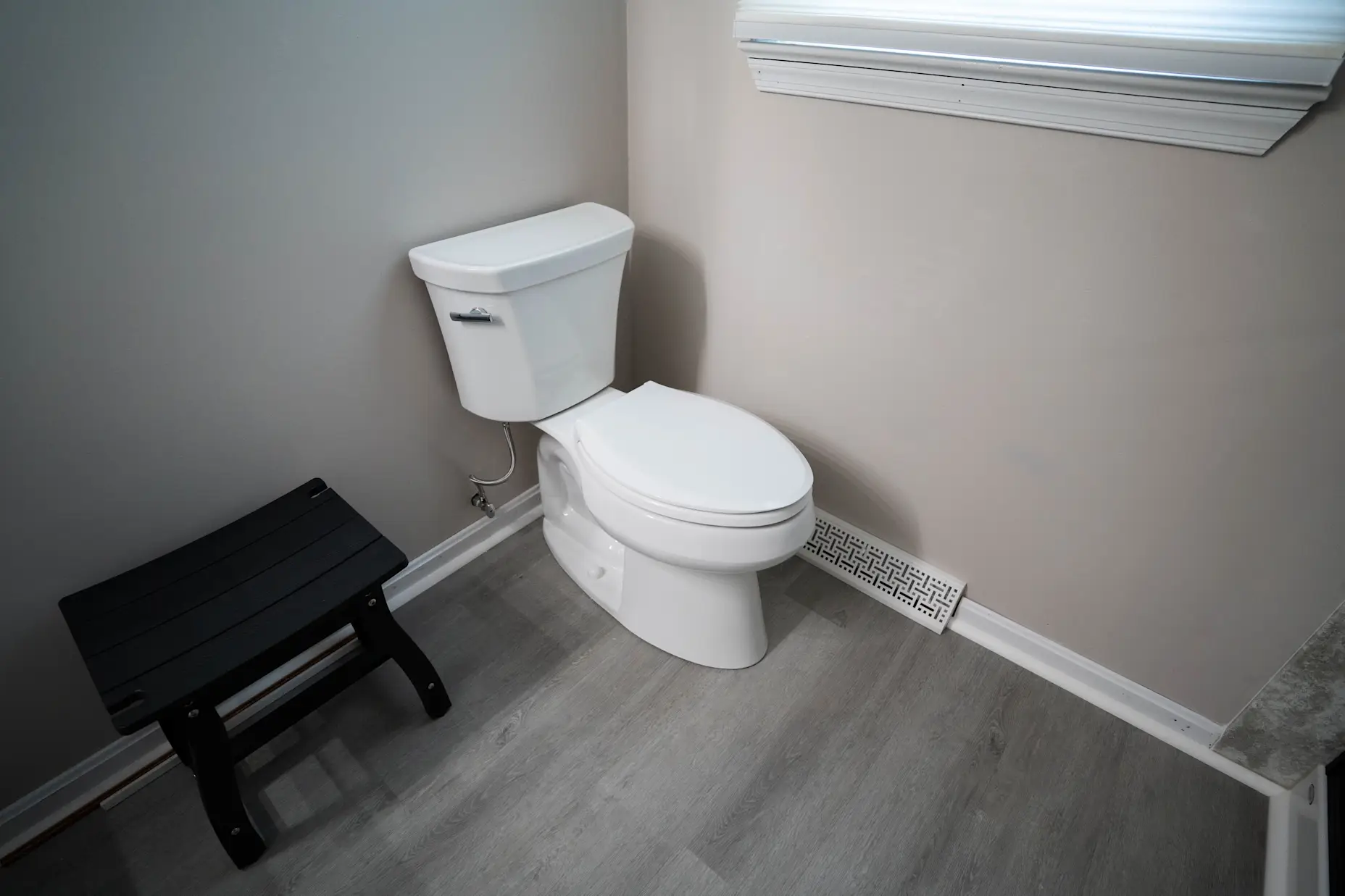 A white Kohler toilet in a grey bathroom.