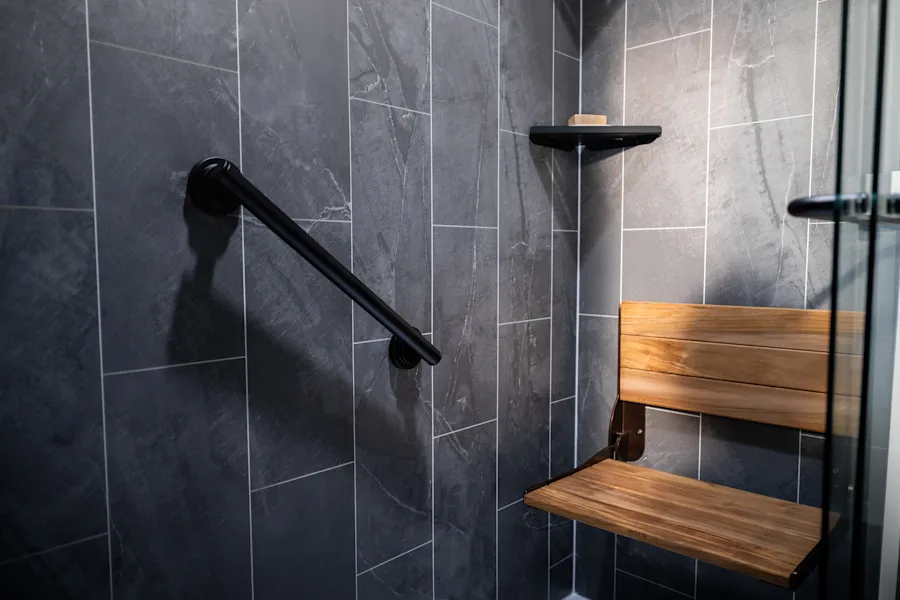 Close detail of an Iron Quarry Nexa shower wall with a matte-black grab bar and teak fold-down seat
