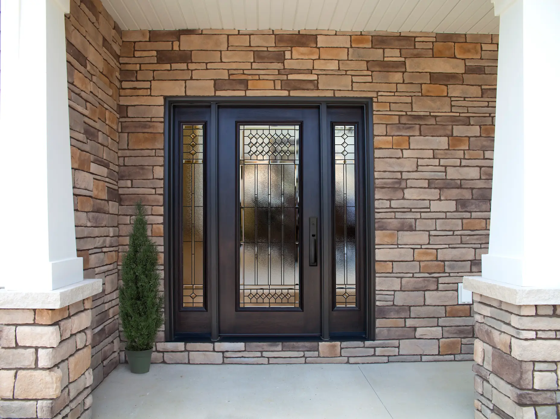 A black single entry door on a home with a large porch and bright yellow siding.