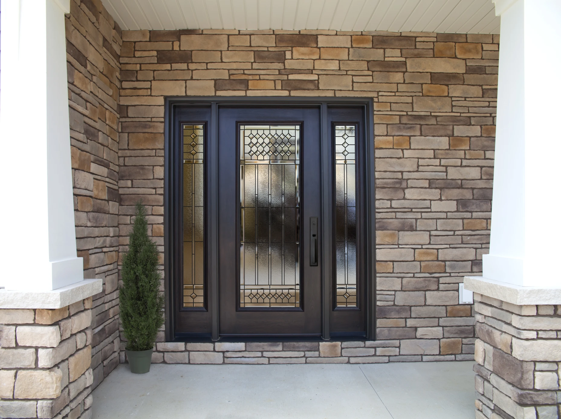 A black single entry door on a home with a large porch and bright yellow siding.