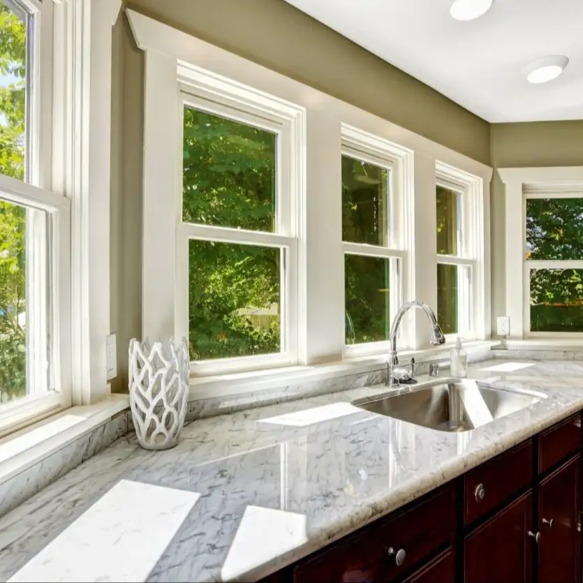 An interior view of a kitchen counter top, sink, and a row of double hung windows.