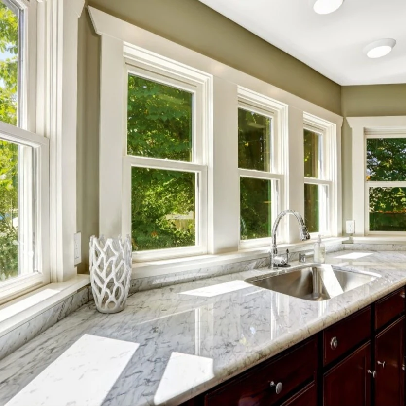 An interior view of a kitchen counter top, sink, and a row of double hung windows.