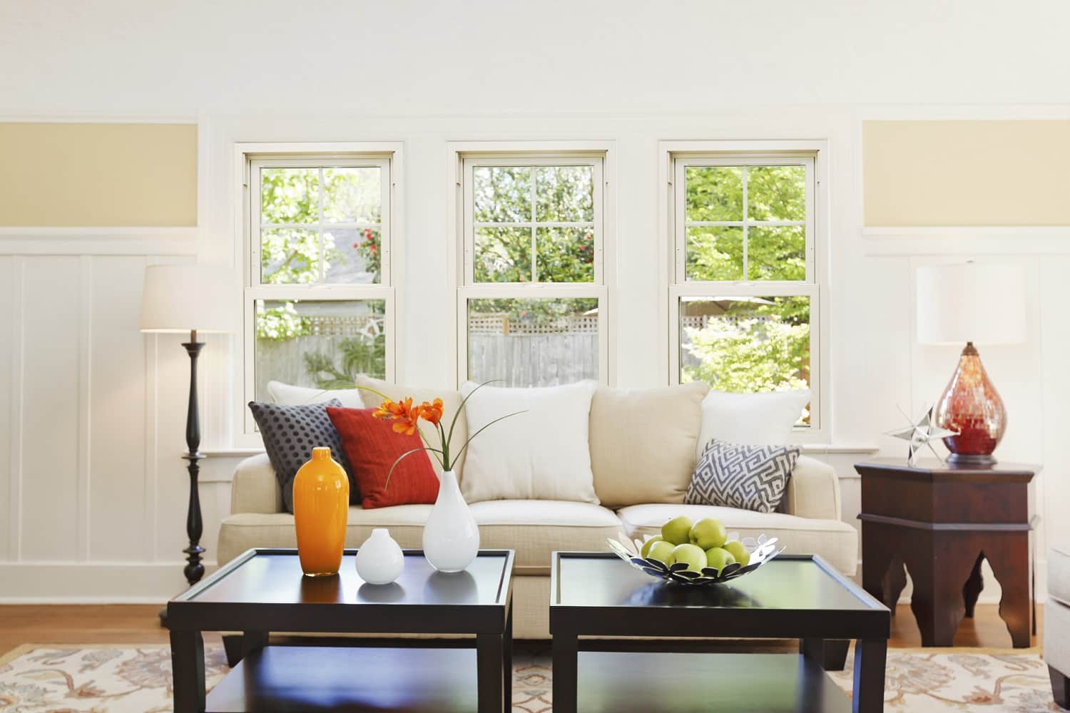 A spacious living room with three double-hung windows looking out onto a yard.