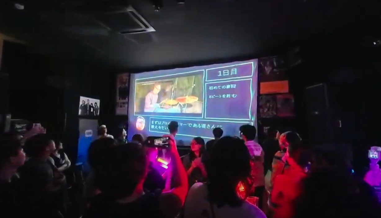 ライブハウスにて、uzさんのドラム練習の軌跡を辿って制作された特別ムービーがスクリーンに流れる様子
