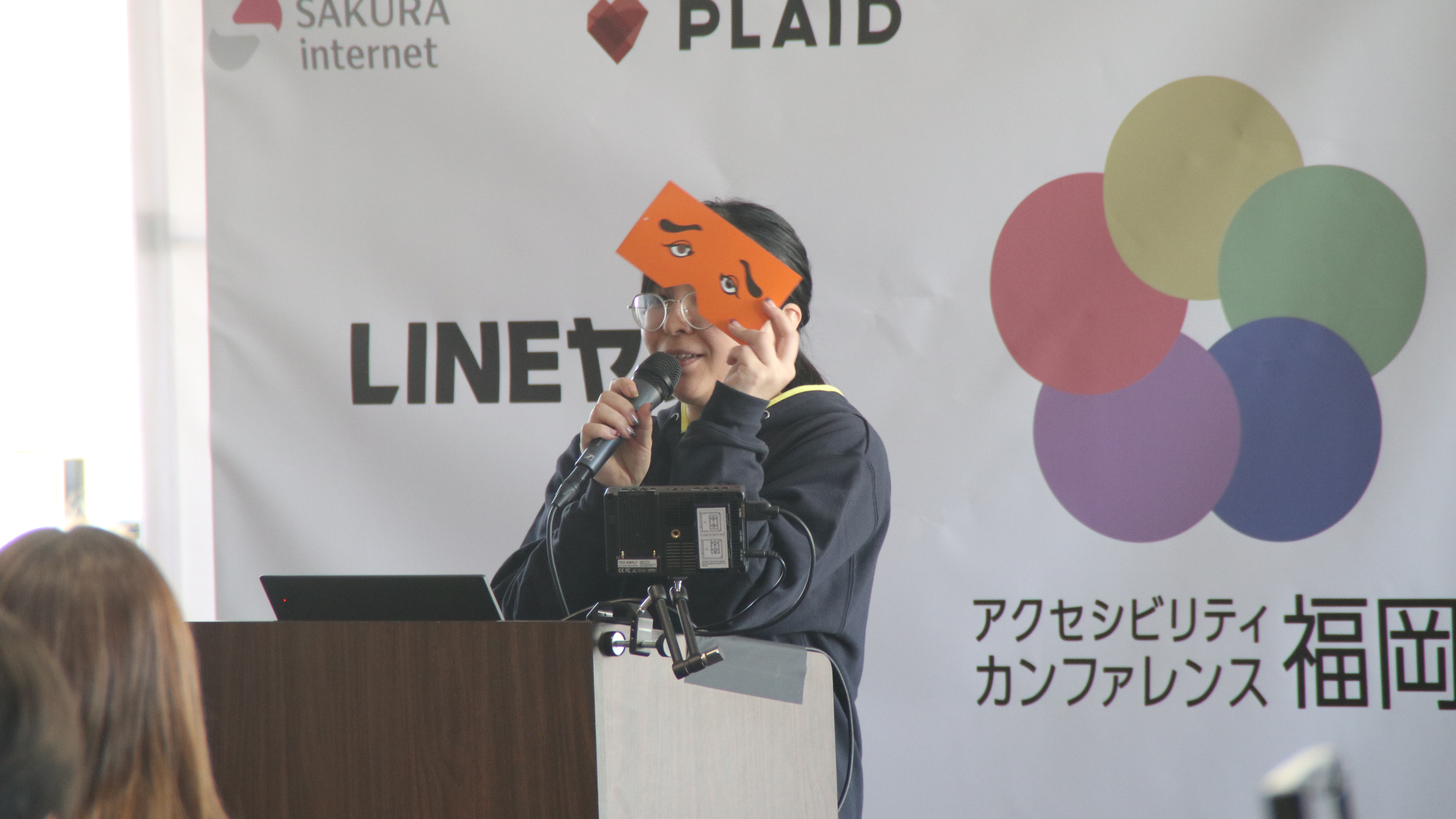 博多名物にわかせんぺいを持ちながらカンファレンスの進行をするミスティさん