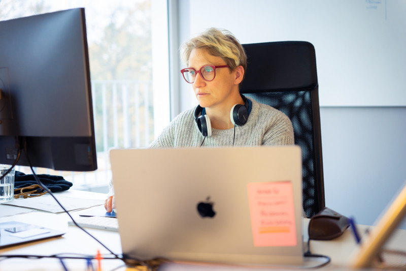 Eine Frau, die hinter einem Computerbildschirm sitzt und sich konzentriert. Sie arbeitet gerade im Potsdamer Office.