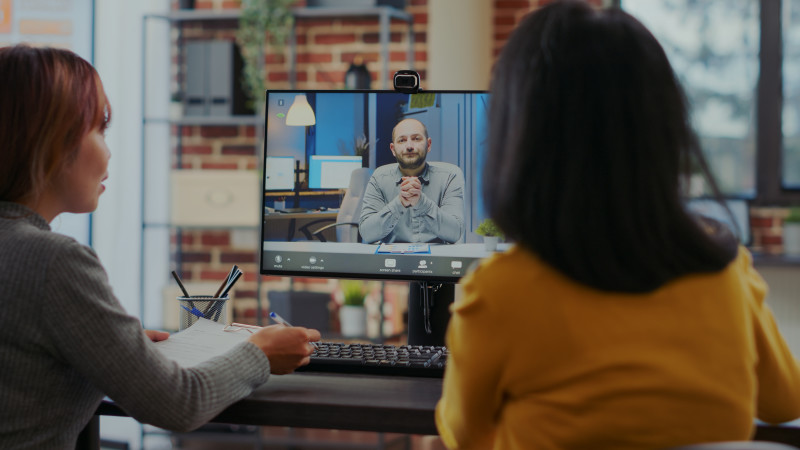 Two interviewers sit in front of a screen. They are in a video call with a user.