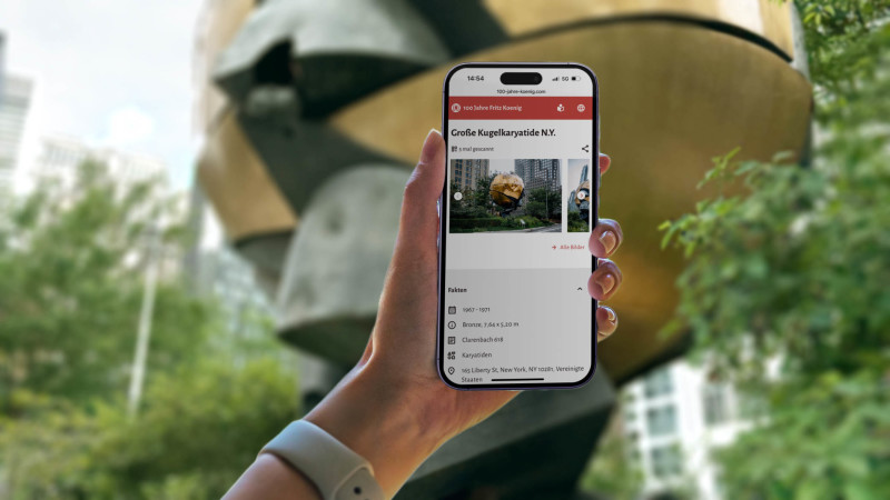 The mobile version of the website in front of the Sphere. It's a bronze sculpture in Liberty Park, New York City.