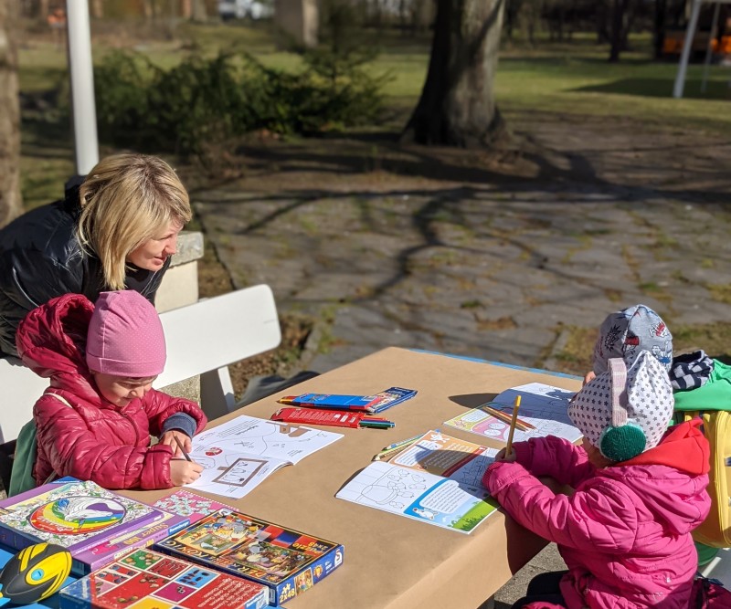 Drei Kinder spielen und malen gemeinsam mit ihrer Mutter im Garten des Kunsthauses Flora. Bild bereitgestellt von Schlaufuchs e.V.