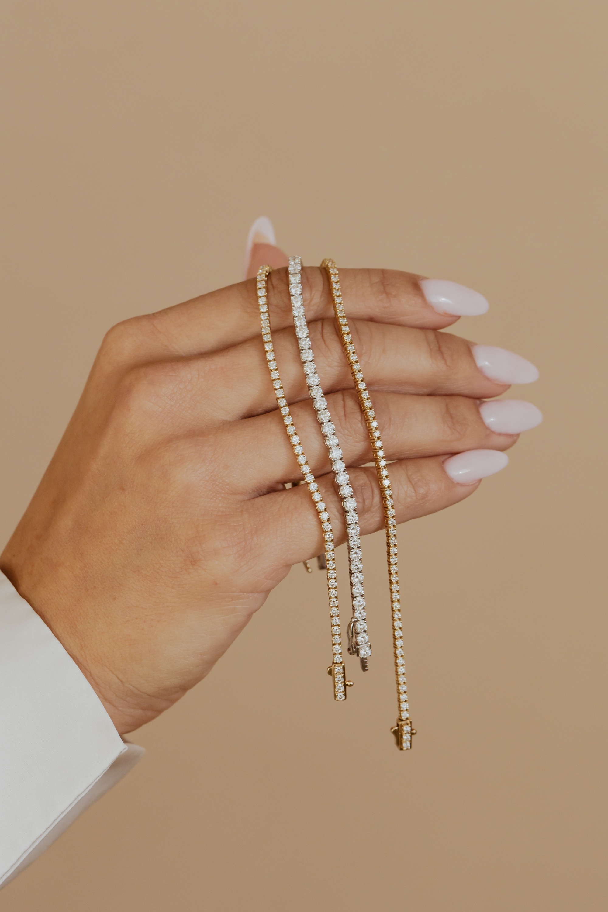 Close up of a woman holding three diamond bracelets with a neutral background.