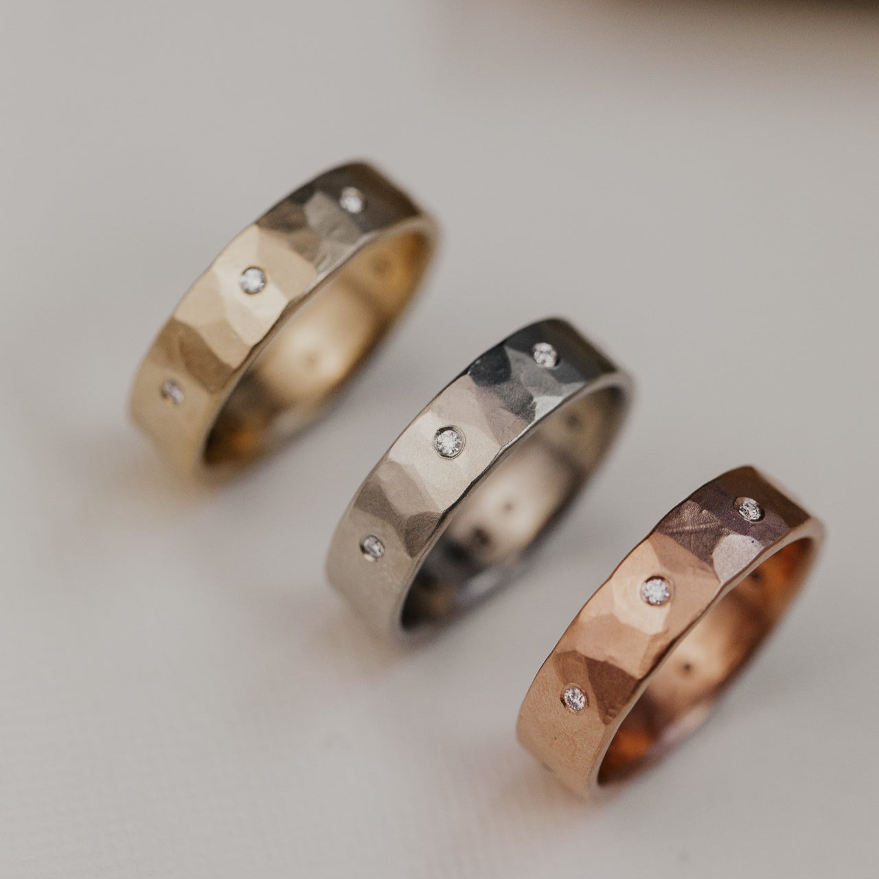 Three Quinn diamond wedding bands in yellow, white, and rose gold on a white background.