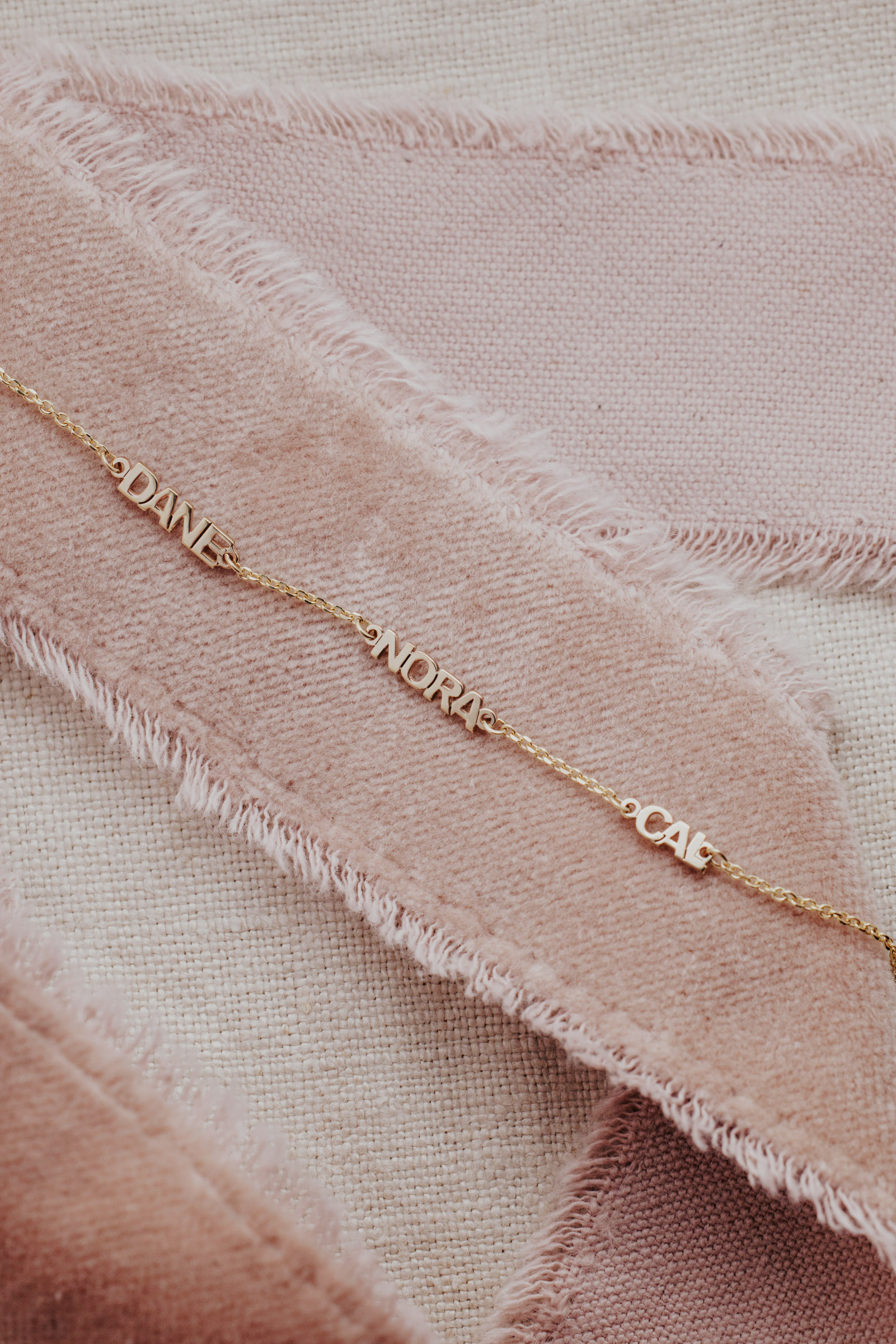 Personalized name bracelet with three names on a pink ribbon.