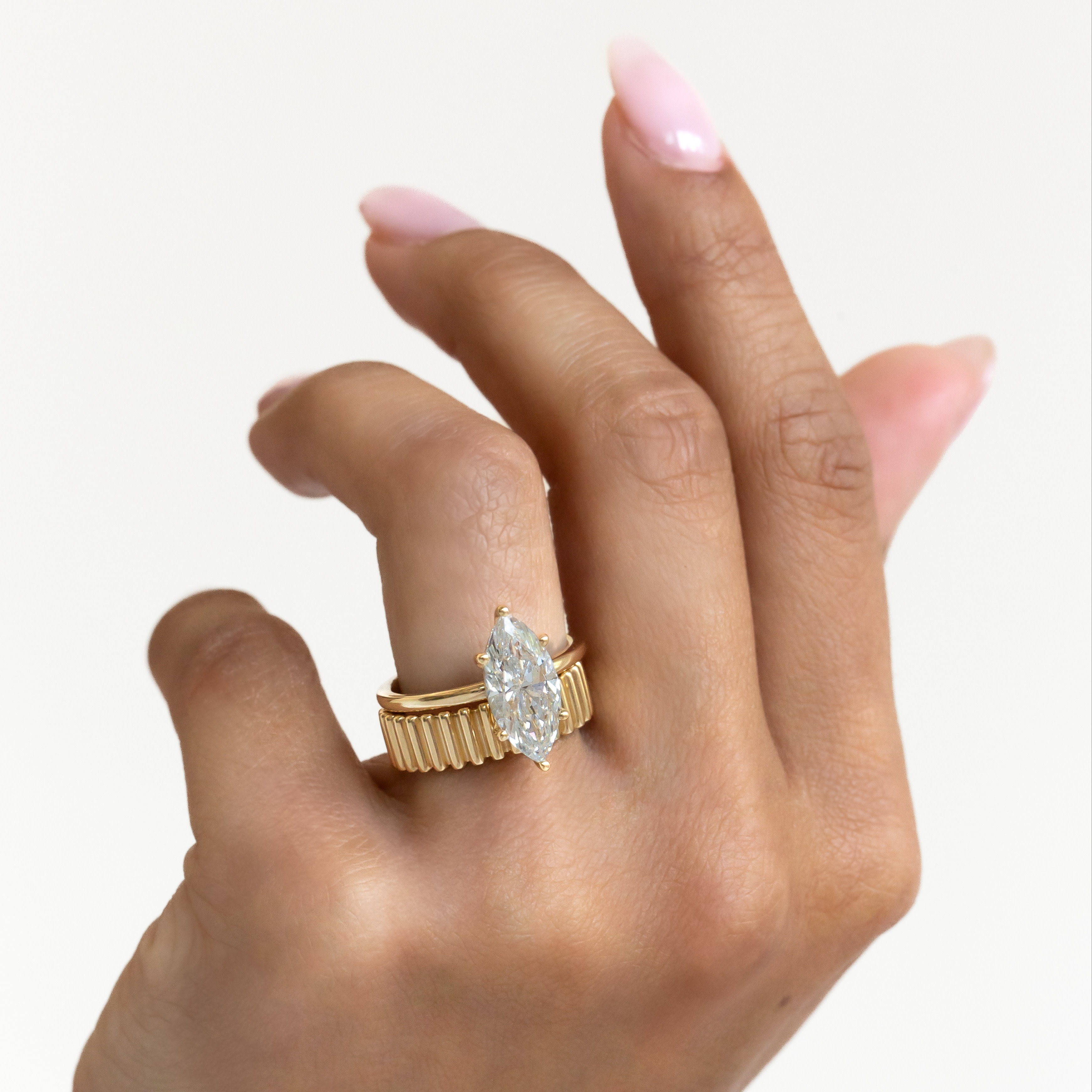 The Maeve marquise diamond engagement ring paired with the drew ribbed gold band on a models hand.