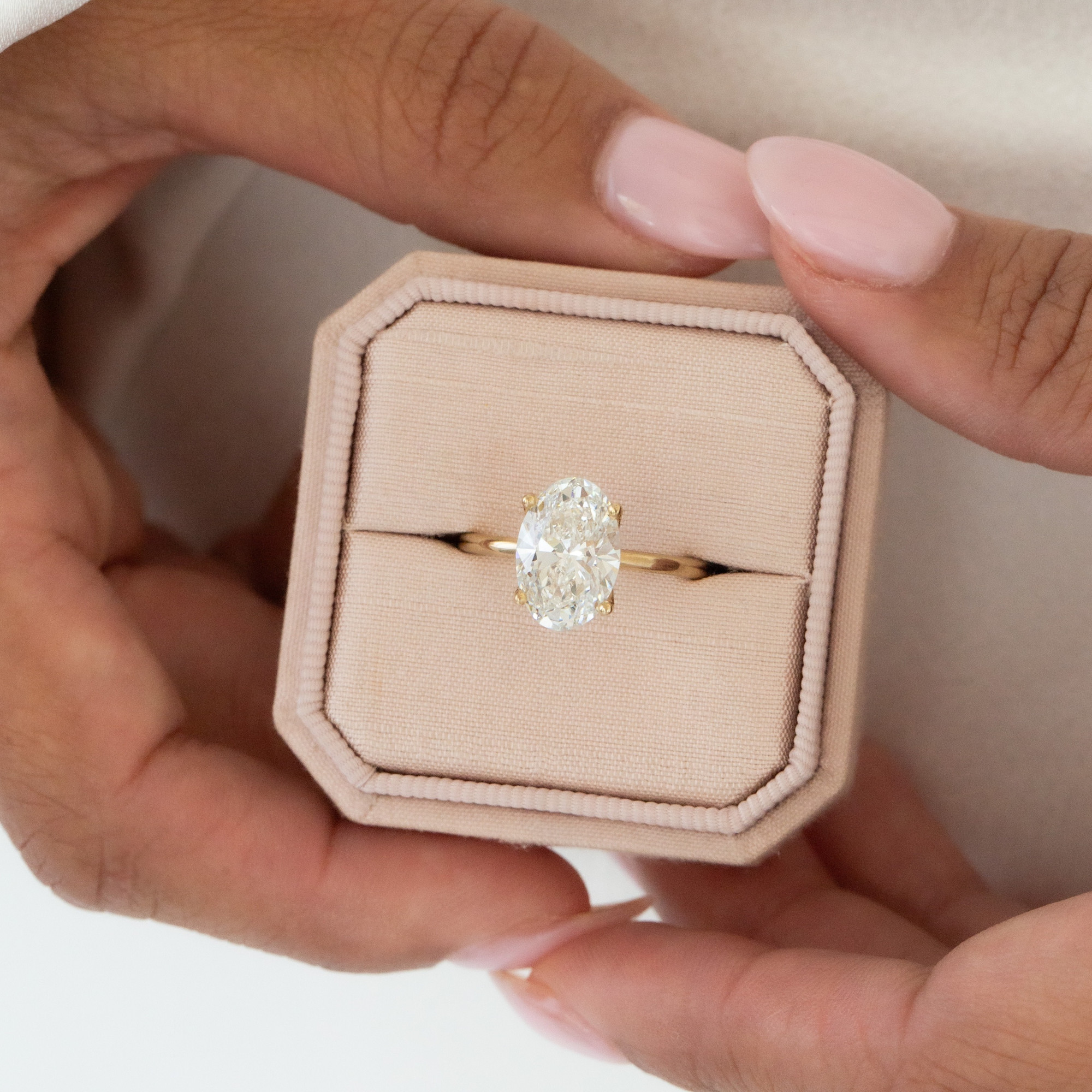 Person holding a light pink ring box with the Maeve oval solitaire diamond ring placed inside.