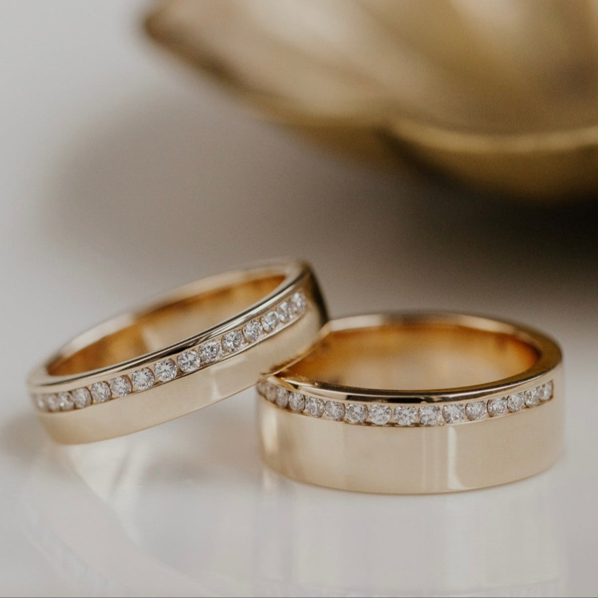 Two gold wedding bands with diamond accents on a neutral background