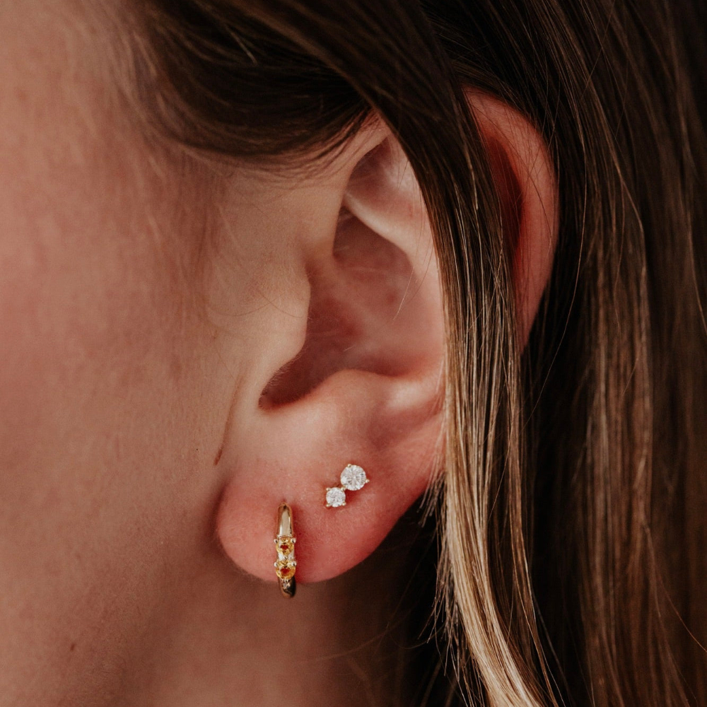 Close-up of an ear wearing gold earrings with a blurred background.