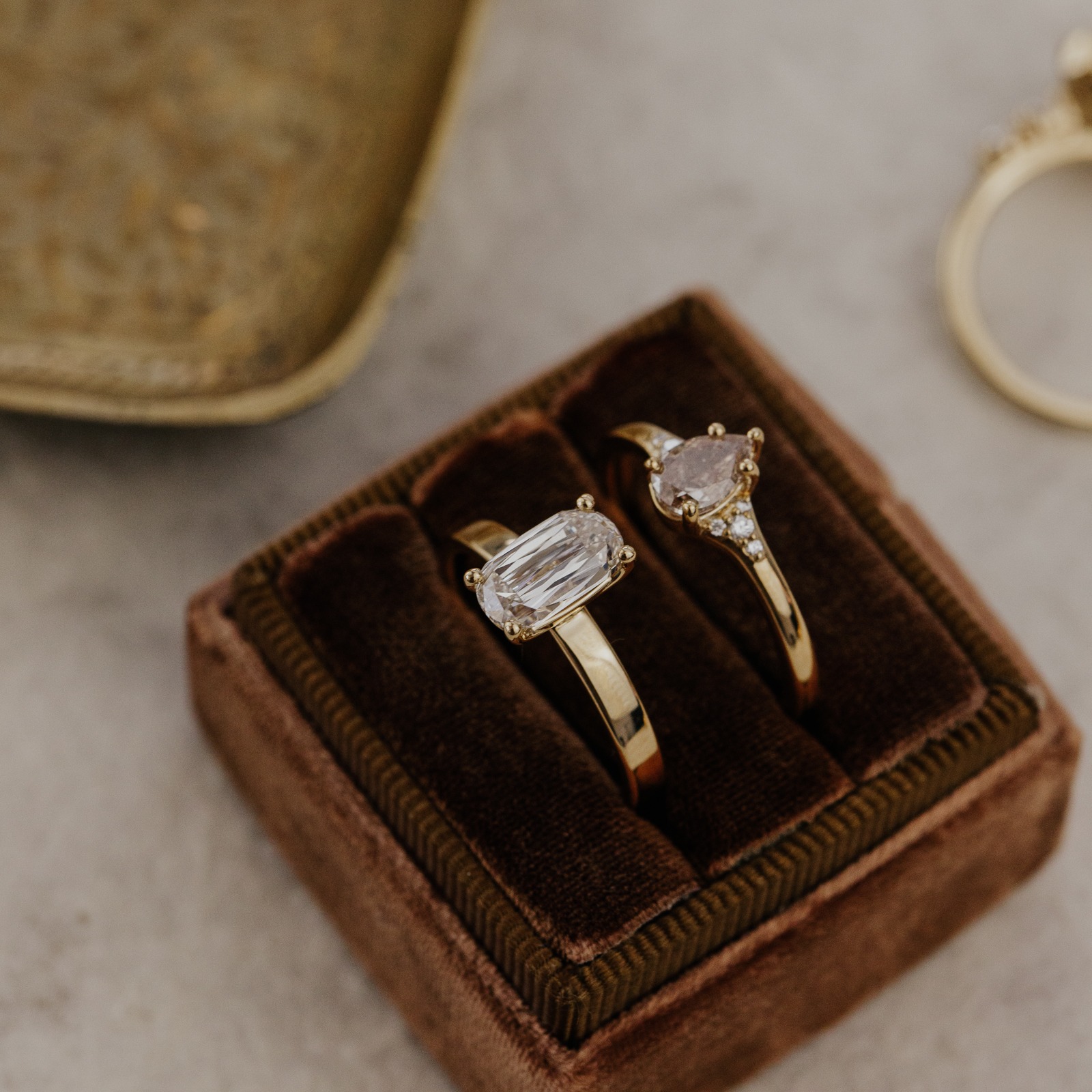 Two champagne diamond engagement rings in a brown velvet ring box.