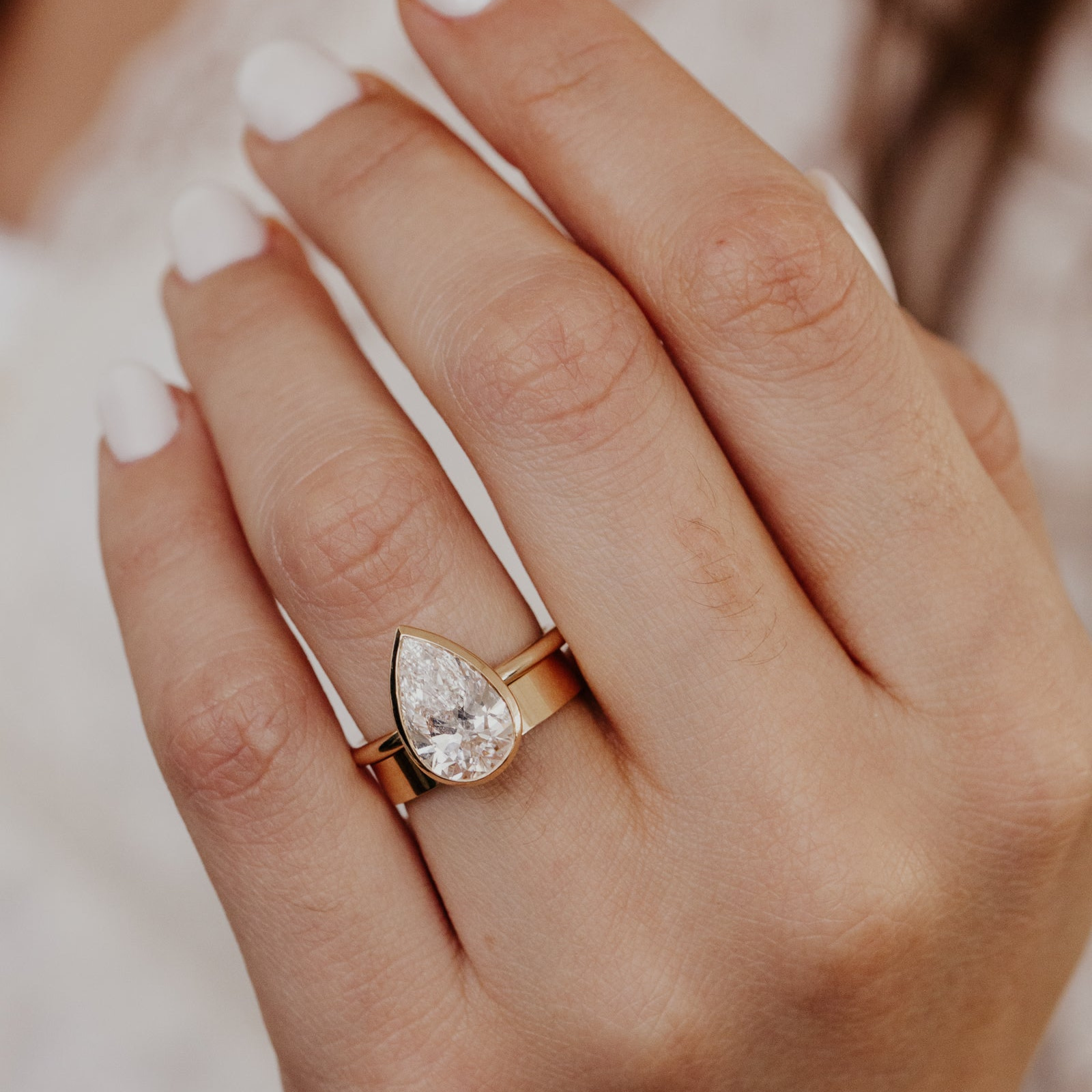 The Bailey pear-shaped diamond engagement ring paired with a gold stacker band on a models hand.