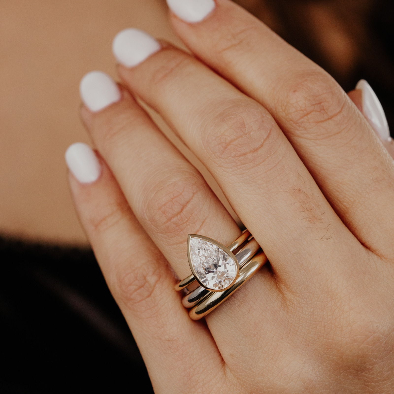 The Bailey pear diamond engagement ring paired with two Maeve bands in white and yellow gold on a models hand.