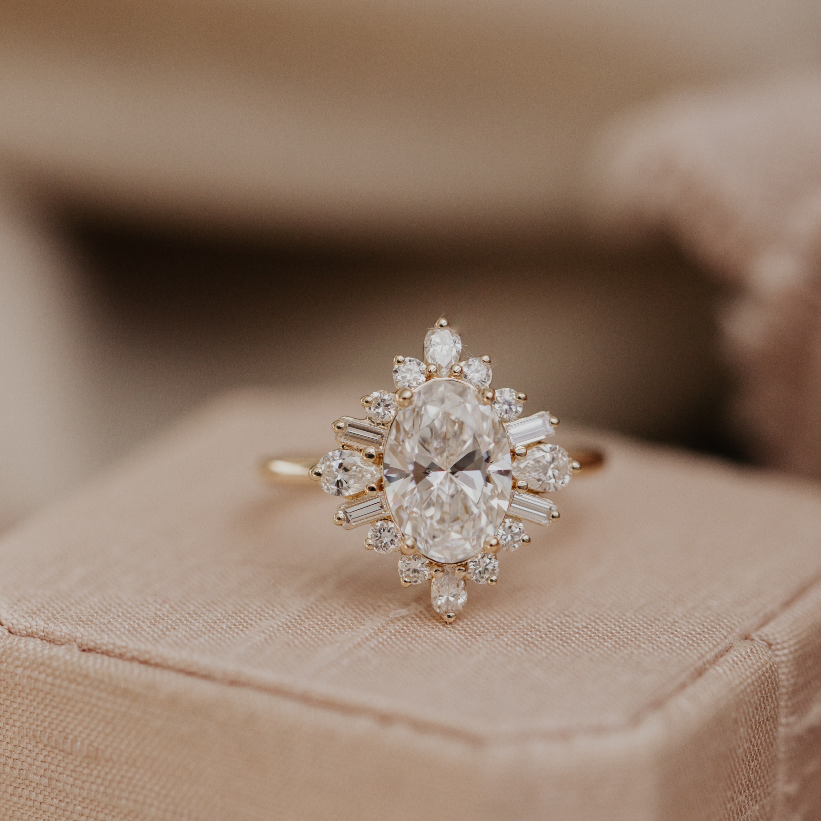 The Harlem oval engagement ring with a round and baguette diamond halo on a light pink ring box with a blurred background.