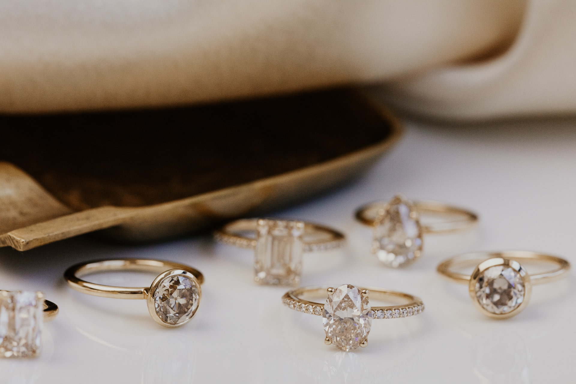 Multiple champagne diamonds in different shapes and settings on a white table.