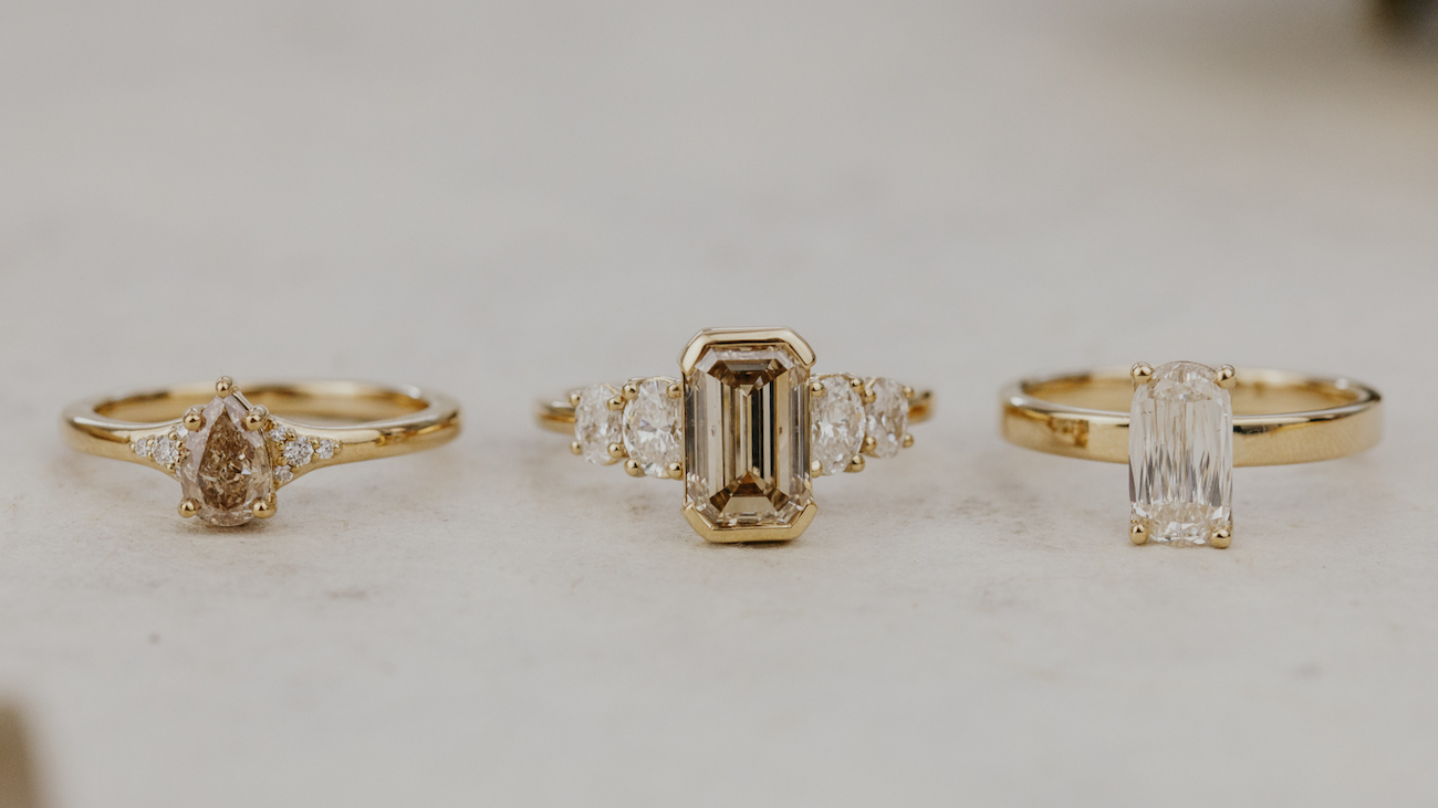Three champagne diamond oval engagement rings on a white surface.
