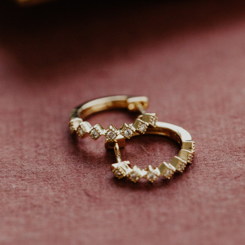 Pair of diamond hoop earrings on a textured red fabric background.