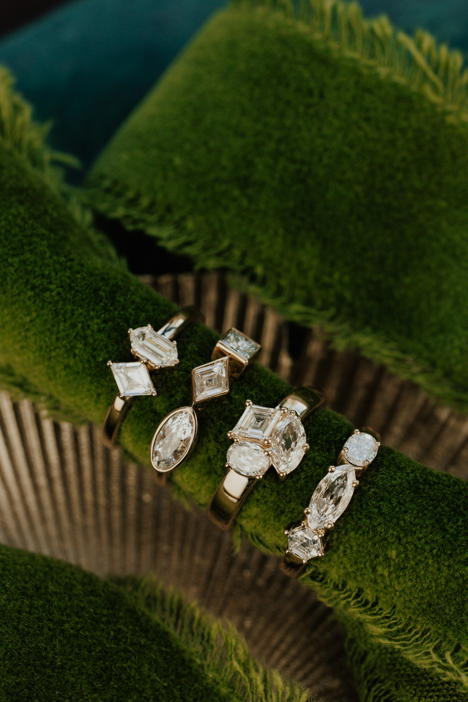 Four diamond cluster rings on a green fabric.