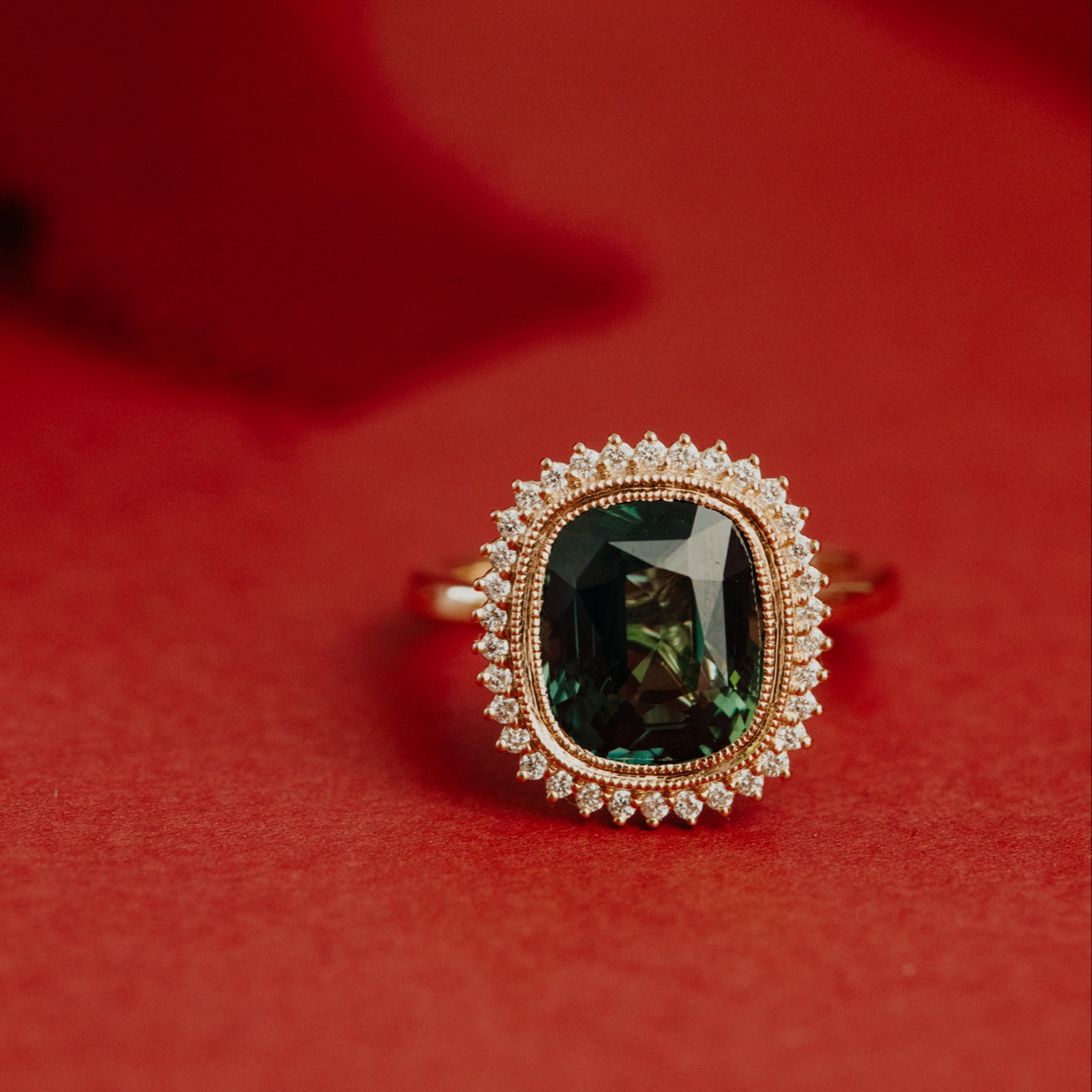 Green sapphire engagement ring with a diamond halo on a red festive background