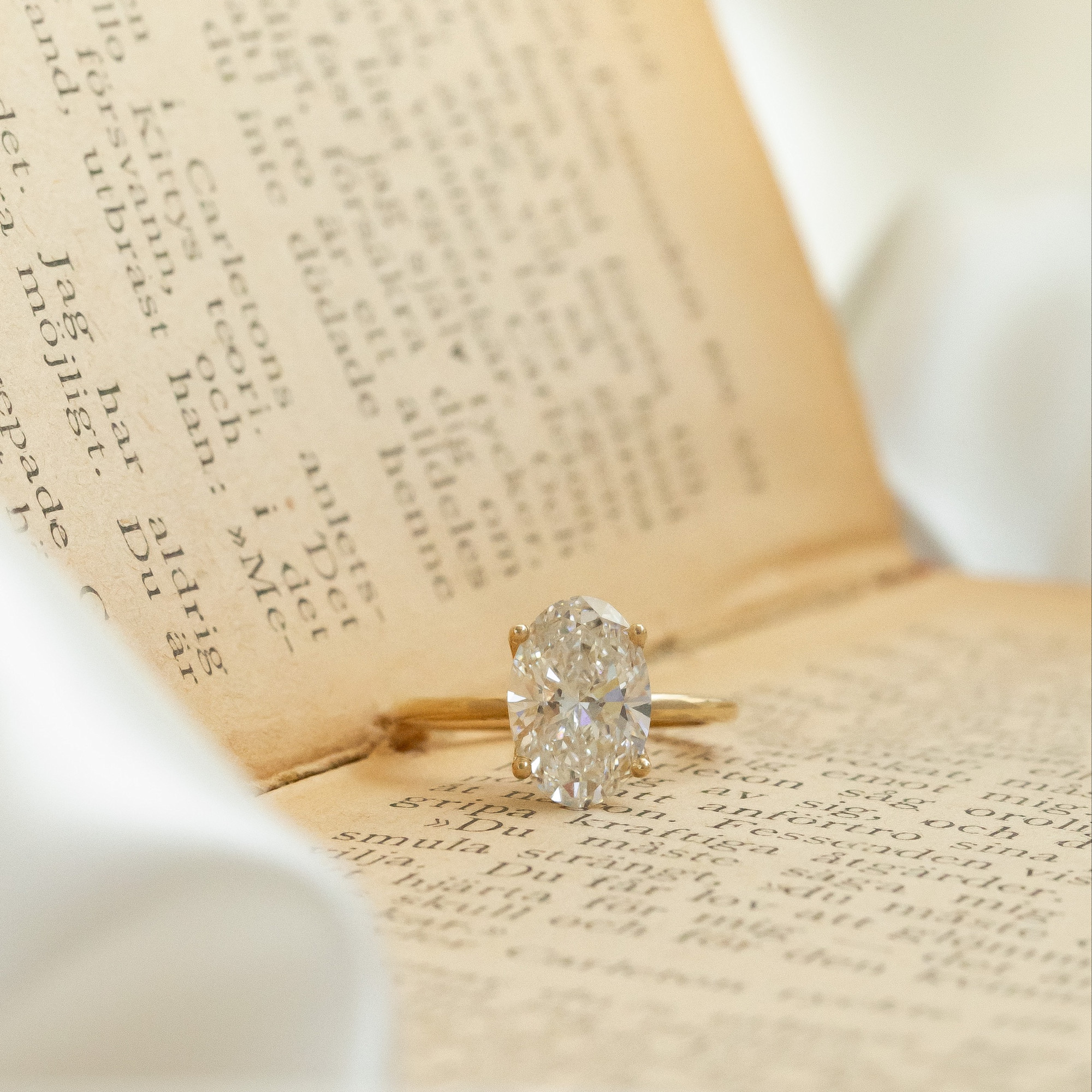 The maeve oval diamond solitaire ring placed on a open book.