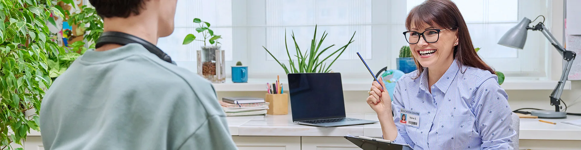 Young adult and provider sitting in an examine room by a desk with a clipboard smiling and talking.