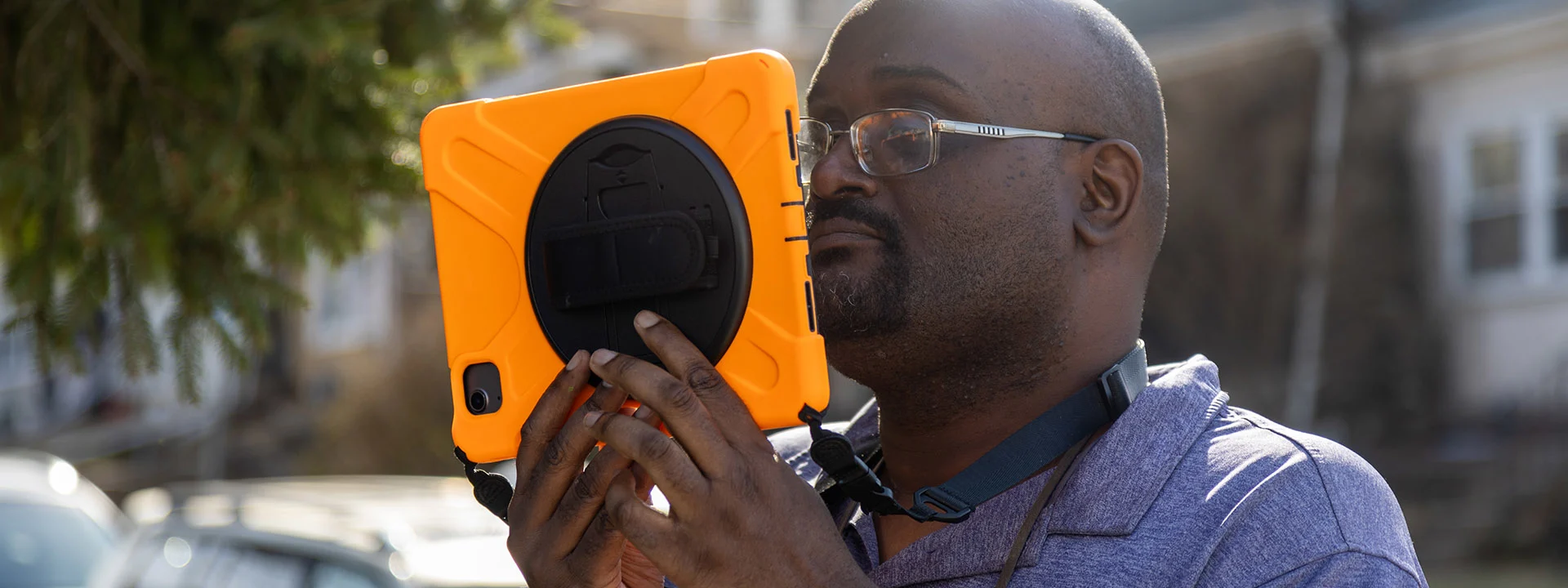 Adult male wearing glasses holding an iPad close to his face and looking at the device screen.