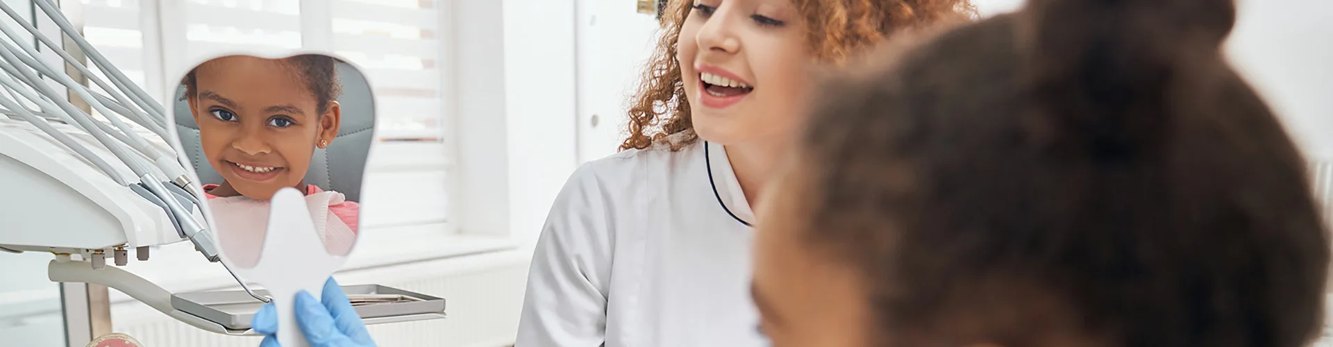 Primary care provider holding a hand held mirror up to Childs face with child's smile reflected back in the mirror.