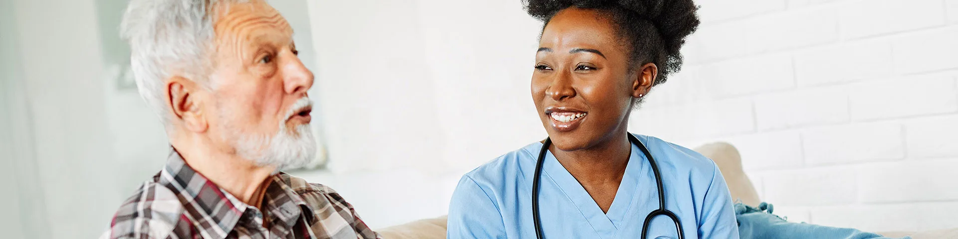 Elderly patient sitting and talking with nurse holding a clipboard