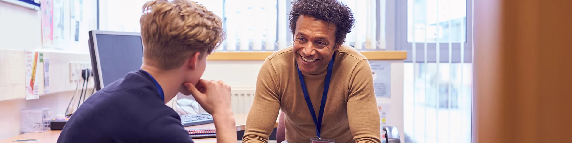 Young person and adult mentor sitting in an office by a desk with an open laptop smiling and talking