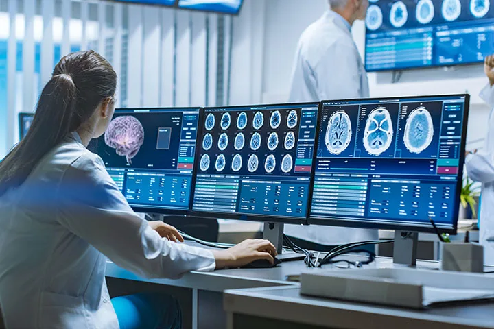 Medical professional looking at brainscans on three monitors