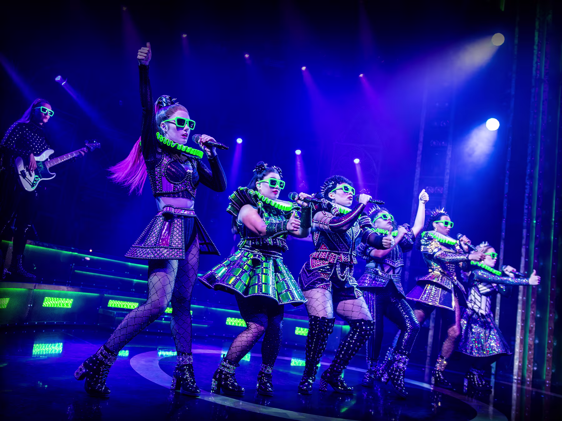 Foto aus dem Musical Six: Königinnen stehen auf der Bühne mit blauer Beleuchtung und singen mit ihren Mikrofonen. 