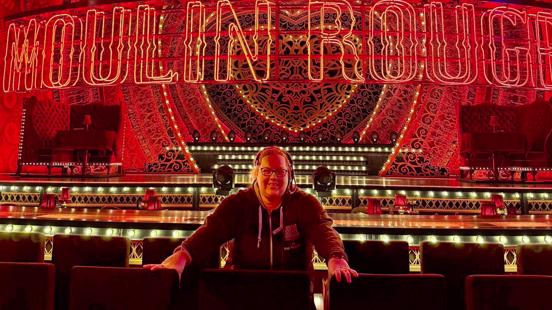 Frau zwischen den Zuschauerreihen vor dem Bühnenbild von Moulin Rouge! Das Musical